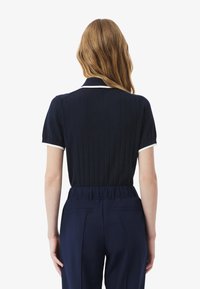 Polo à manches courtes côtelé marine avec des accents de col blanc, présentant un design ajusté. Le dos montre une texture lisse et une finition sans coutures.