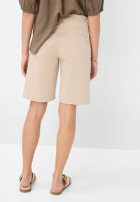 Beige, knielange shorts met een losse pasvorm, gemaakt van zacht materiaal. Kenmerken zijn een elastische tailleband en twee achterzakken.