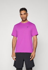Rövid ujjú, kerek nyakú póló élénk lila színben, puha, könnyű anyagból. A mellkasán egy kis fekete Nike logó található.