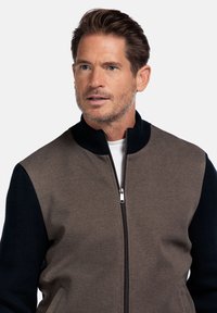 Heren zip-up jack met een bruine body, marineblauwe gebreide mouwen, geribbelde kraag en voorzakken. Strak design met ritssluiting.