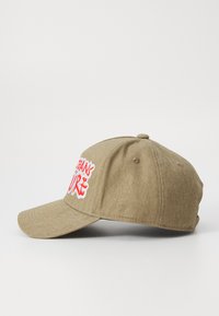 Casquette de baseball en khaki fabriquée en tissu texturé, avec un texte rouge brodé bien visible sur le côté et une visière incurvée.