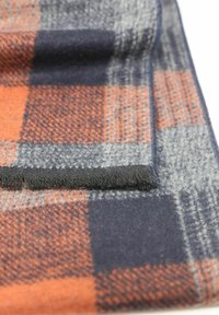 Écharpe en laine pliée avec un motif à carreaux dans des couleurs orange, bleu marine, noir et gris, montrant un gros plan de son tissu doux et texturé.