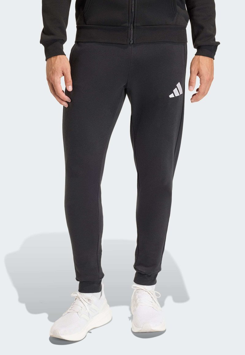 Μαύρο αθλητικό παντελόνι από λείο ύφασμα, με στενή εφαρμογή, ελαστικά μανσέτα και λευκό λογότυπο Adidas στο μηρό.