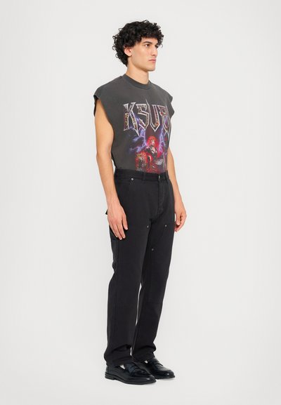 Black graphic t-shirt with short sleeves and a colorful design, paired with black pants featuring a straight cut and side pockets. Black shoes.