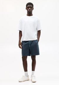 Weißes T-Shirt mit kurzen Ärmeln, navyfarbene Shorts mit Kordelzug und weiße Sneaker. Glatter Stoff, lockere Passform, schlichtes Design.
