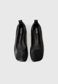 Ballerines en cuir noir avec un design à bout carré. Texture lisse, petit talon et petite languette à l'arrière. L'intérieur présente un marquage.