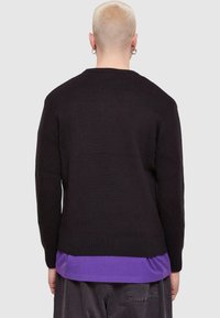 Pulover negru tricotat cu guler rotund, manșete și tiv cu dantelă, suprapus peste un tricou purpuriu. Textură moale, croi relaxat și design minimalist.