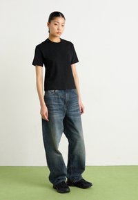 Camiseta negra de manga corta, jeans de mezclilla azul sueltos con un acabado desgastado y zapatillas deportivas negras. Diseño simple, corte relajado, estilo casual.