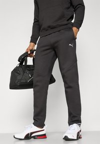 Sorte, atletiske joggers med en slank pasform, prydet med et lille hvidt logo, parret med hvide og sorte sneakers samt en sort duffelbag.