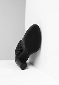 Czarna szpilka z siateczkowym cholewką, teksturowaną podeszwą i solidnym obcasem. Posiada włoską markę i geometryczny wzór na podeszwie.