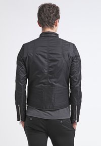 Svart skinnmotorcykeljacka med en strömlinjeformad design, texturerat tyg, vadderade detaljer och synliga blixtlås på ärmarna.