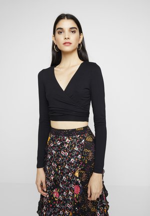 Top cropped preto de mangas longas com um decote em V profundo e um design envolto. Combinado com uma saia de padrão floral multicolorido com babados.