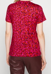 T-shirt à manches courtes de couleur rose vif avec un motif léopard en noir et rouge. Tissu doux avec une coupe décontractée.