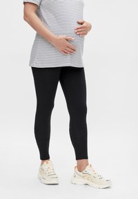 Fekete leggings csíkos pólóval, formázott dizájnnal. Fehér sportcipővel kombinálva, narancssárga részletekkel. Sima textúra, laza stílus.