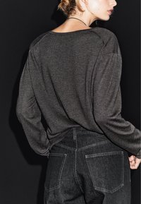 Šedý dlouhý rukáv top z měkké látky, charakterizovaný volným střihem a širokým výstřihem, zkombinovaný s tmavými džínami s vysokým pasem a kapsami.