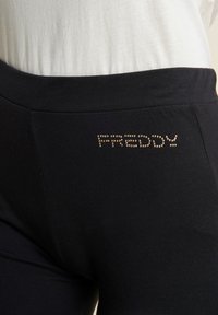 Leggings neri elasticizzati con una texture liscia, caratterizzati dalla parola "FREDDY" in borchie metalliche sulla vita.
