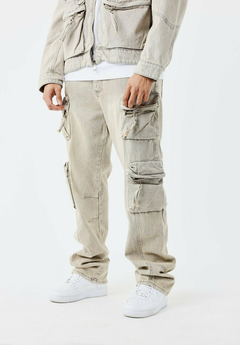 Ljust grå cargobyxor med flera fickor med dragkedja, lös passform och elastiska mudd, kombinerat med vita sneakers. Strukturerat denim-material.