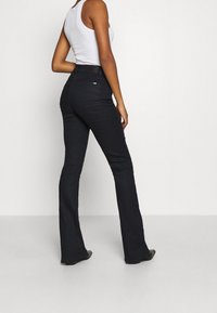 Mustat levenevät farkut, joissa on keskikorkea vyötärö, klassinen viiden taskun malli ja hienovaraiset saumaukset. Sileä farkkukangas.