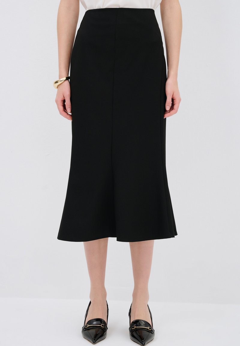 Schwarzer Midirock mit ausgestelltem Saum, aus glattem Stoff. Kombiniert mit spitzen schwarzen Schuhen und einem schlichten weißen Oberteil. Elegante Silhouette.