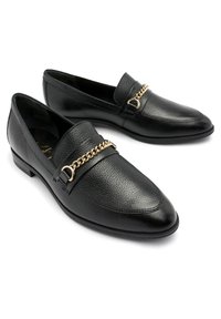 Mocassins en cuir noir avec une finition texturée, dotés d'un accent en chaîne dorée et d'un bout légèrement pointu. Talon bas et design à enfiler.