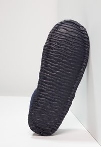Zwarte rubberen zool met een getextureerd, golvend patroon; heeft een blauwe bovenkant; ontwerp is laagprofiel en instap.