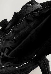 Innensicht einer schwarzen Tote Tasche, die ein Reißverschlussfach und ein weiches Innenfutter zeigt, wobei die Geräumigkeit und das gestepptes Design betont werden.