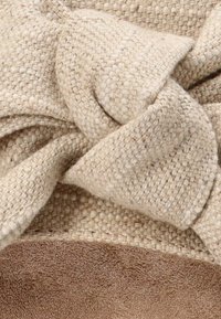 Tela tejida beige con una superficie texturizada, que presenta un destacado detalle de nudo. La sección inferior muestra un suave ante de color marrón claro.