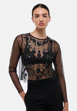 Haut transparent noir à manches longues, présentant des perles noires délicates et des broderies florales, superposé sur une couche inférieure noire unie.