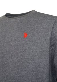 Szürke crewneck pulóver, bal mellrészen egy kis piros hímzett logóval, amely egy lóháton ülő pólózót ábrázol.
