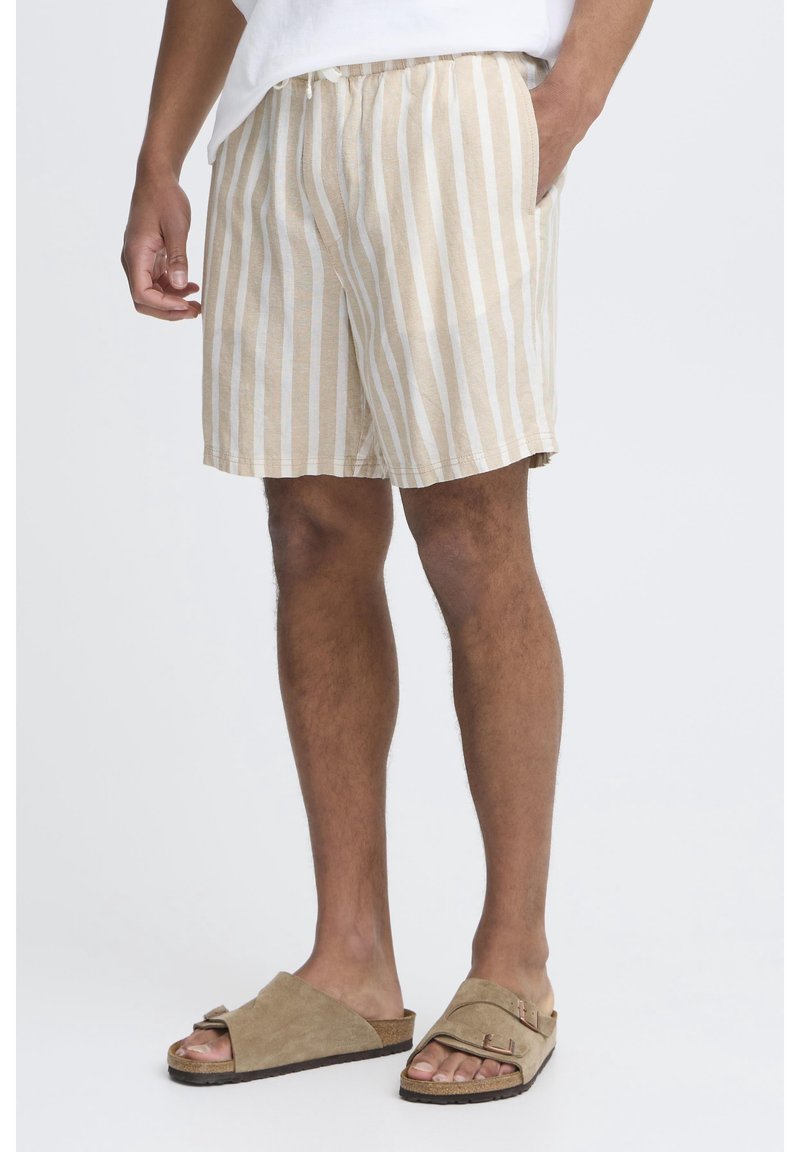 Shorts en lin rayés beige et blanc avec une taille élastique, des poches latérales et une coupe décontractée, associés à des sandales à glisser marron clair.