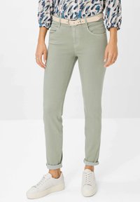 Helle grüne, enganliegende Jeans mit glatter Textur, ausgestattet mit fünf Taschen und einem passenden Gürtel. Getragen mit weißen Sneakern und umgekrempelten Bündchen.