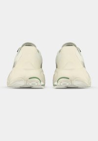 Ζευγάρι ανοιχτόχρωμων αθλητικών παπουτσιών, εμφανιζόμενα από πίσω, με παχιά σόλα που διαθέτει κυκλικά σχέδια για καλύτερη πρόσφυση και διακριτικές πράσινες λεπτομέρειες.