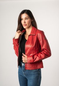 Rode leren jack met een gestructureerde kraag, ritsluiting en voorknoopzakken. Gedragen over een zwarte top, gecombineerd met blauwe jeans. Gladde textuur.
