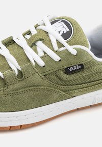 Zöld szarvasbőr sneaker fehér fűzőkkel és fekete Vans logóval a nyelvén. Texturált oldalsó panellel és gumis talppal rendelkezik.