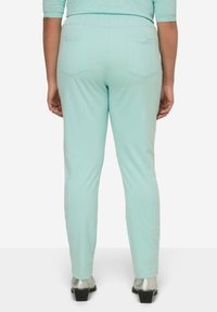 Pantalones elásticos color verde menta con un diseño ajustado, que cuentan con dos bolsillos traseros y una cinturilla elástica, combinados con botas metálicas hasta el tobillo.