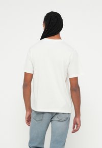 Tricou alb din bumbac, cu un croi lejer, mâneci scurte și gât rotund, având un tiv drept și detalii de cusătură minime.