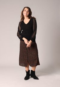 Schwarzer Strickpullover mit Netzärmeln, kombiniert mit einem schwarzen Rock mit rotem Punkte-Muster und schwarzen Wildleder-Stiefeletten.