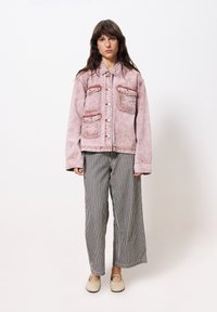 Rosa Denimjacke mit zwei vorderen Taschen, getragen über weit geschnittenen schwarz-weißen gestreiften Hosen. Einfache flache beigen Schuhe runden das Outfit ab.