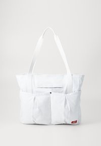 White fabric tote bag with a flat top, two long handles, and an external pocket featuring pleats and a logo. Smooth texture, minimalist design.