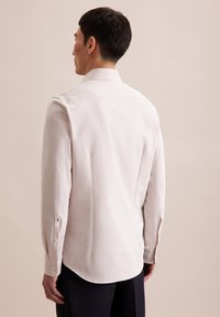 Lichtbeige button-up shirt met een zachte textuur, voorzien van een klassieke kraag, een taps toelopende achterkant en knopen op de manchetten, gecombineerd met donkere broek.