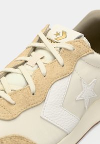 Hvide sneakers med beige ruskindselementer, prydet med et struktureret læderstjerne-logo, cremede snørebånd og guldbranding på tungen.