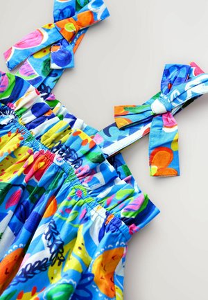 Robe colorée avec une base bleue, taille élastique et tissu à motifs présentant des fruits et des fleurs. Bretelles à nœud réglables.