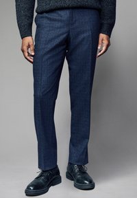 Sötétkék, szabott nadrág, texturált mintával, slim fit fazonban és lapos elülső résszel. Fekete fűzős dresszcipővel párosítva.