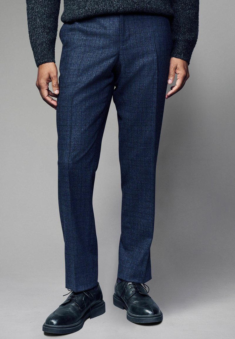 Sötétkék, szabott nadrág, texturált mintával, slim fit fazonban és lapos elülső résszel. Fekete fűzős dresszcipővel párosítva.
