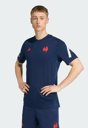 T-shirt de sport navy avec un logo de coq rouge et trois rayures rouges sur l'épaule gauche. Fabriqué à partir d'un tissu lisse et respirant.