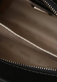 Intérieur d'un sac noir à fermeture éclair avec finition texturée. Doublure en tissu clair exposée, montrant une couleur beige, des bords cousus et une quincaillerie en or.