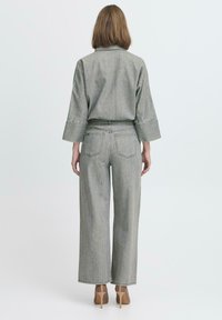 Szürke farmer összeállítás, amely hosszú ujjú, galléros felsőt és bőszárú nadrágot tartalmaz. Texturált anyag, látható varrással és két hátsó zsebbel.