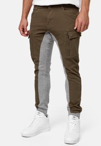 Cargo pants featuring a mix of olive green and grey fabric, slim fit, multiple side pockets, and cuffs with elastic detailing.