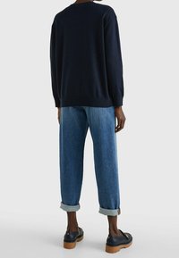 Marineblauwe trui met geribbelde onderrand en manchetten, gecombineerd met lichtblauwe jeans met omgeslagen onderkant en zwarte instapschoenen met houten zolen.