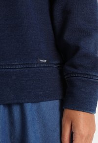 Marineblaue Sweatshirt mit strukturiertem Stoff, gerippten Bündchen und sichtbarem Markenlabel nahe dem Saum. Schlichtes, lässiges Design.